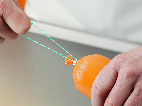 Photo d’une personne tenant une saucisse d’une main et la ficelle de l’autre, afin d’illustrer la pose automatique de ficelle sur les saucisses