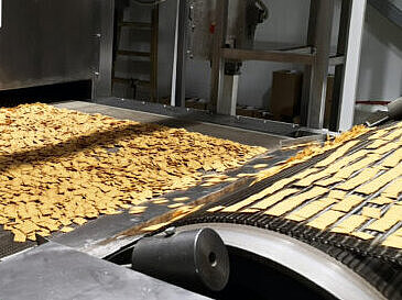 Image d’aliments alignés sur un tapis de production, illustrant les étapes de décongélation ou de cuisson