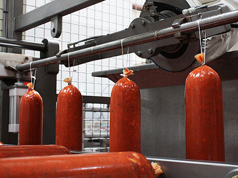 Saucisses accrochées sur un rail métallique en inox, illustrant la dépose automatique de ficelles